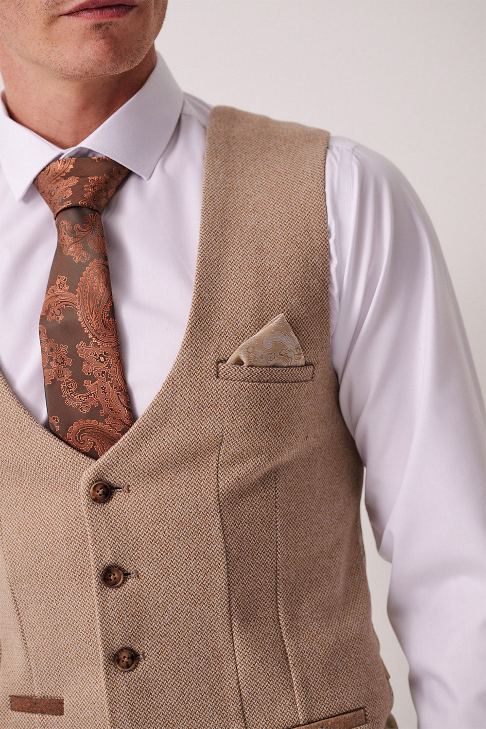 A man wears the Marc Darcy HAYDEN - Oak Crossweave Waistcoat over a white dress shirt, paired with a paisley brown tie and matching pocket square. The image is cropped at the mouth and mid-torso.