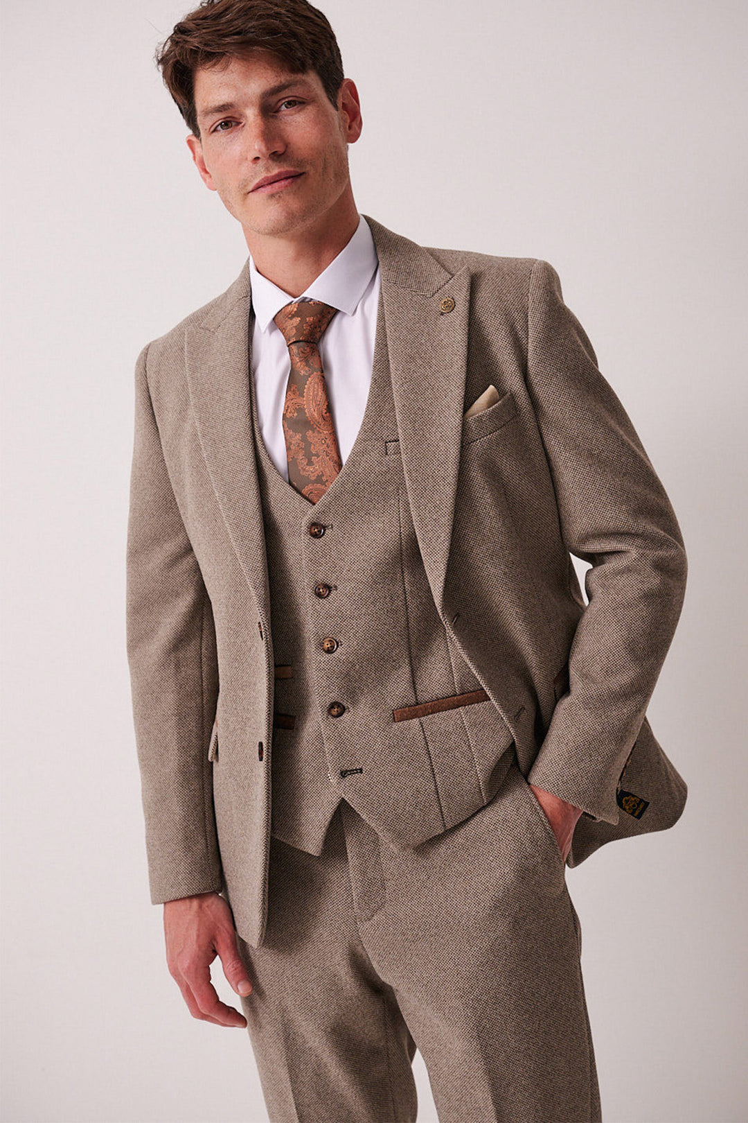A man wearing the marcdarcy HAYDEN - Tan Crossweave Blazer with a matching vest, white shirt, and patterned brown tie stands against a plain light background, looking confidently at the camera.
