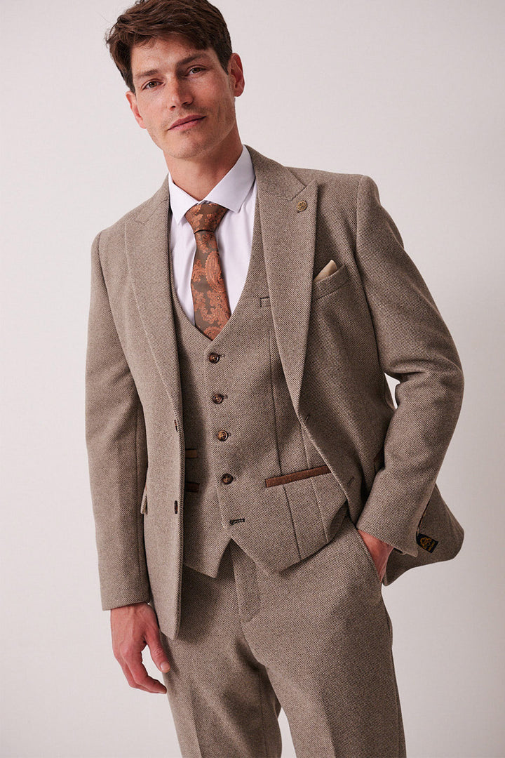 A man wearing the marcdarcy HAYDEN - Tan Crossweave Blazer with a matching vest, white shirt, and patterned brown tie stands against a plain light background, looking confidently at the camera.