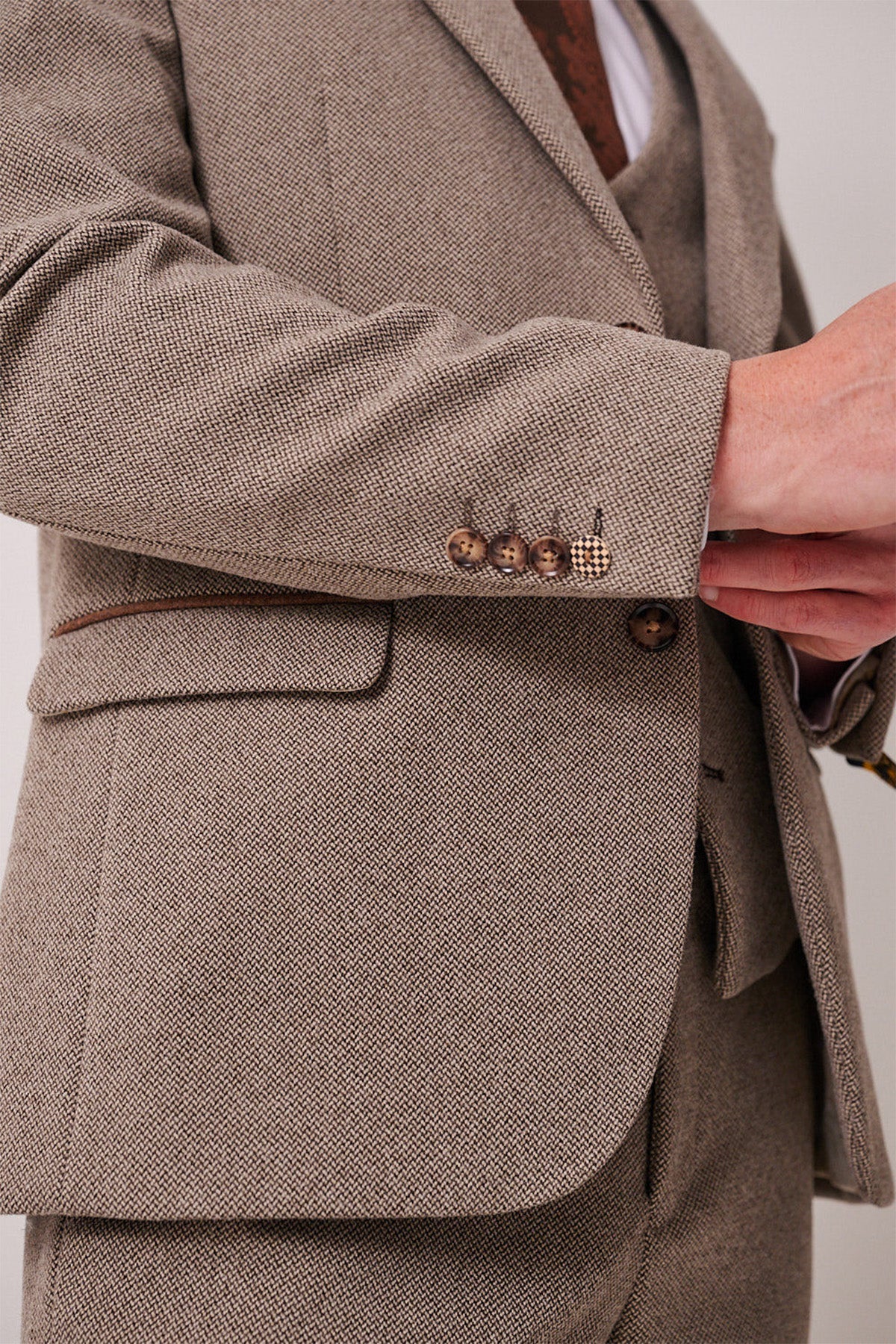 A close-up of a person in the marcdarcy HAYDEN Tan Crossweave Blazer, adjusting a button and highlighting brown buttons and a pocket flap on the sleeve and jacket.