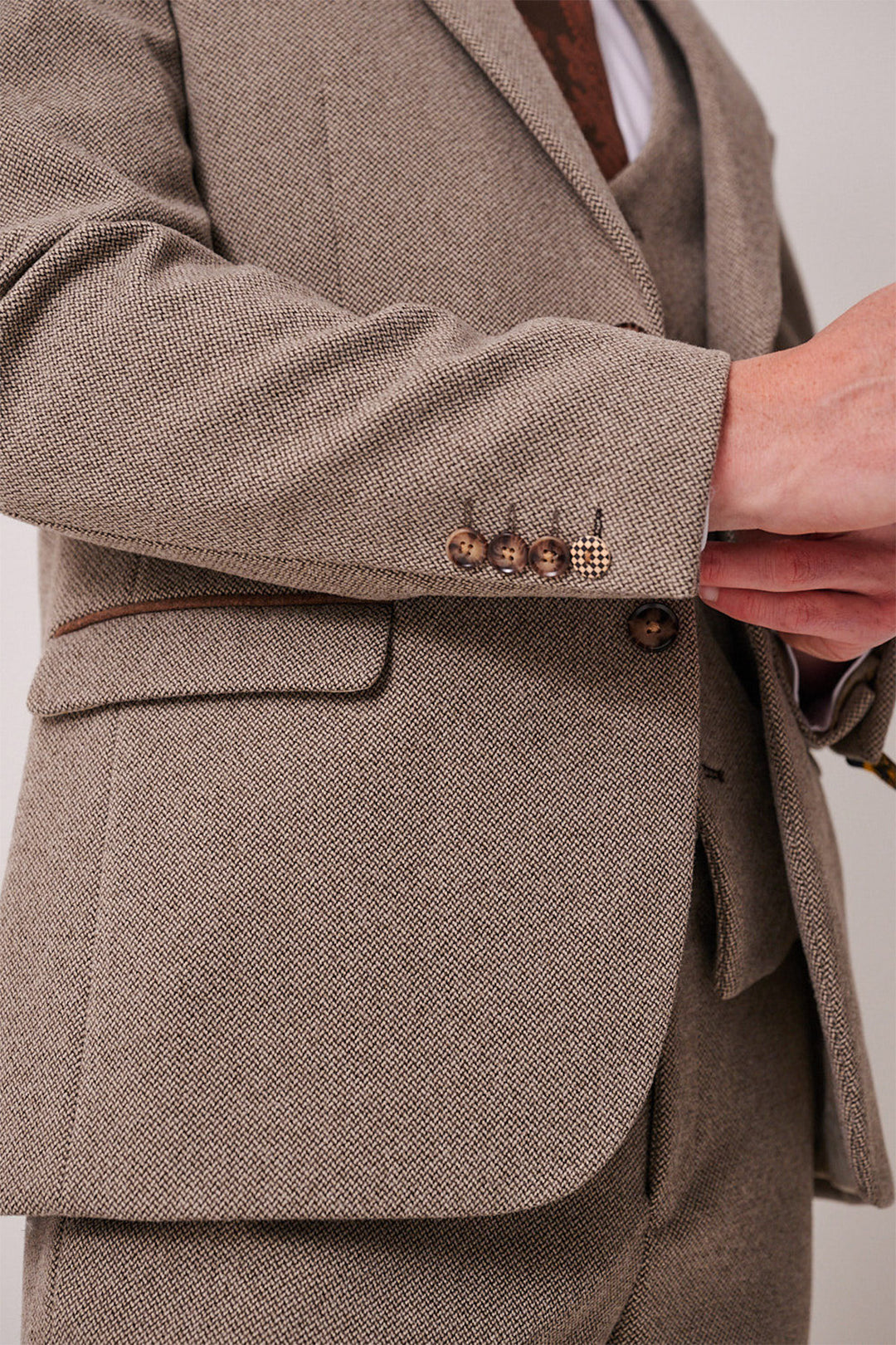 A close-up of a person wearing the marcdarcy HAYDEN Tan Crossweave Three Piece Suit, showing brown sleeve buttons and a hand adjusting the jacket. Only the torso and part of the arm are visible.