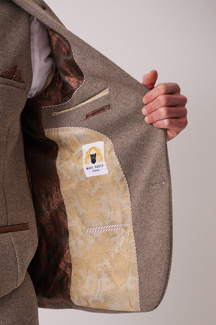 A person holds open the front of a marcdarcy HAYDEN Tan Crossweave Three Piece Suit blazer, showing its ornate golden paisley lining and a label featuring the marcdarcy logo of a man in a hat.