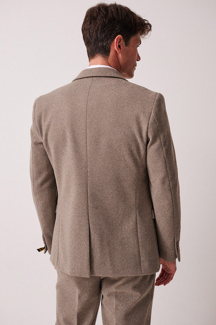 A man wearing the marcdarcy HAYDEN Tan Crossweave Three Piece Suit stands with his back to the camera against a plain, light-colored background.
