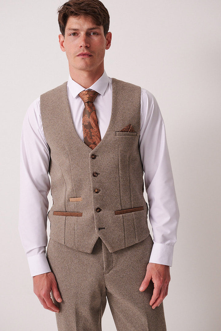 A man wearing the Marc Darcy HAYDEN - Tan Crossweave Waistcoat with matching pants, a white dress shirt, and a brown patterned tie stands facing forward against a plain light background.