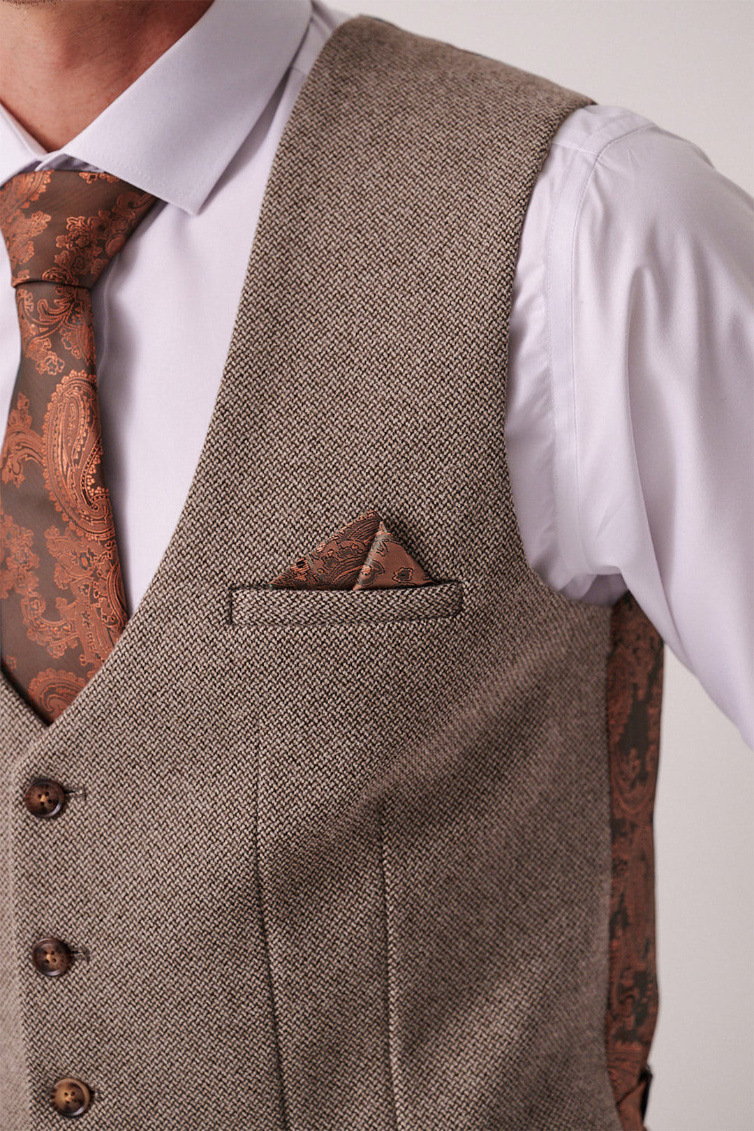 A close-up of a person wearing the marcdarcy HAYDEN Tan Crossweave Three Piece Suit over a white shirt, styled with a brown paisley tie and matching pocket square tucked into the vest pocket.