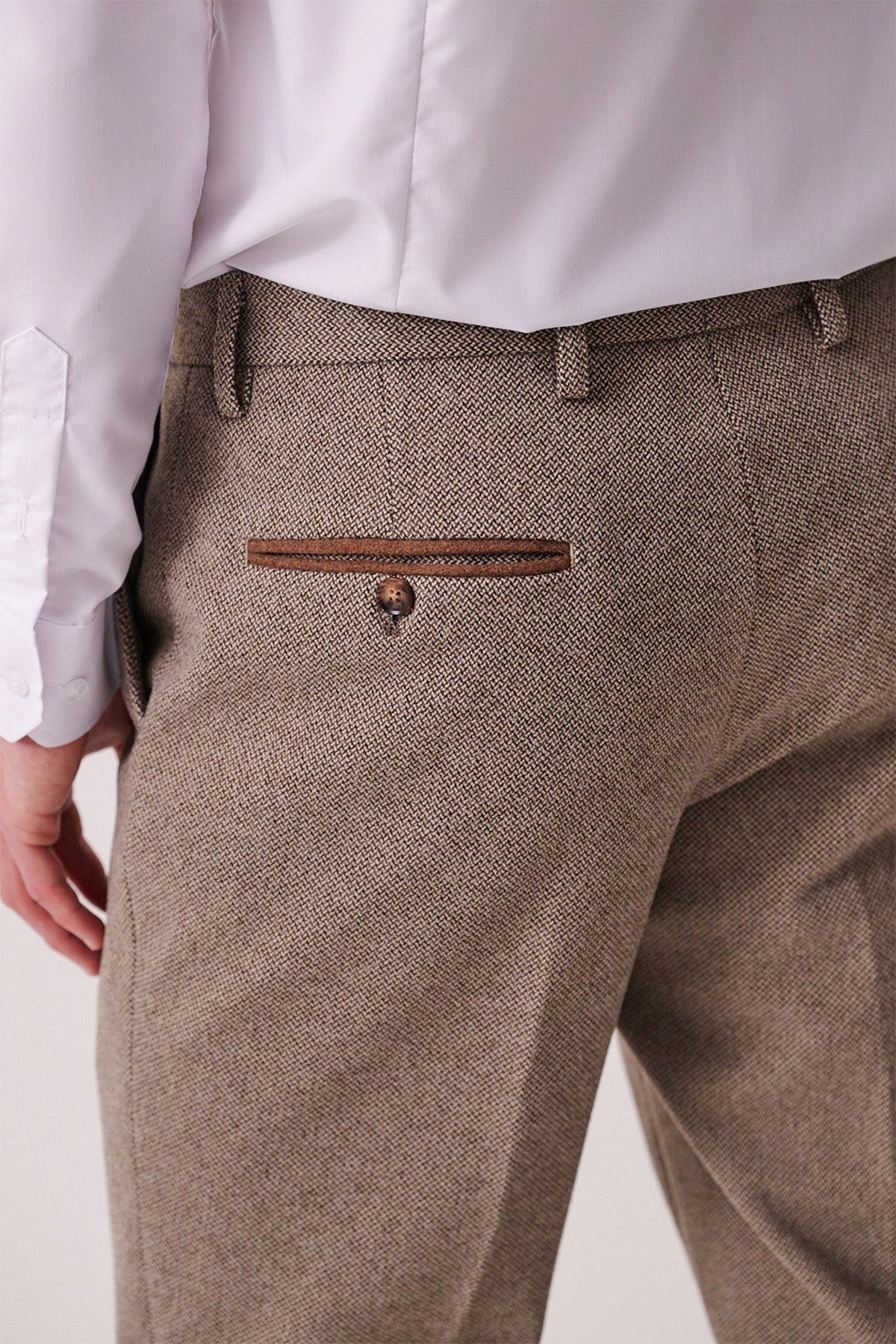A person wearing marcdarcy HAYDEN Tan Crossweave Trousers, featuring a slim fit and buttoned back pocket, paired with a white dress shirt, shown from the waist down in a back view.