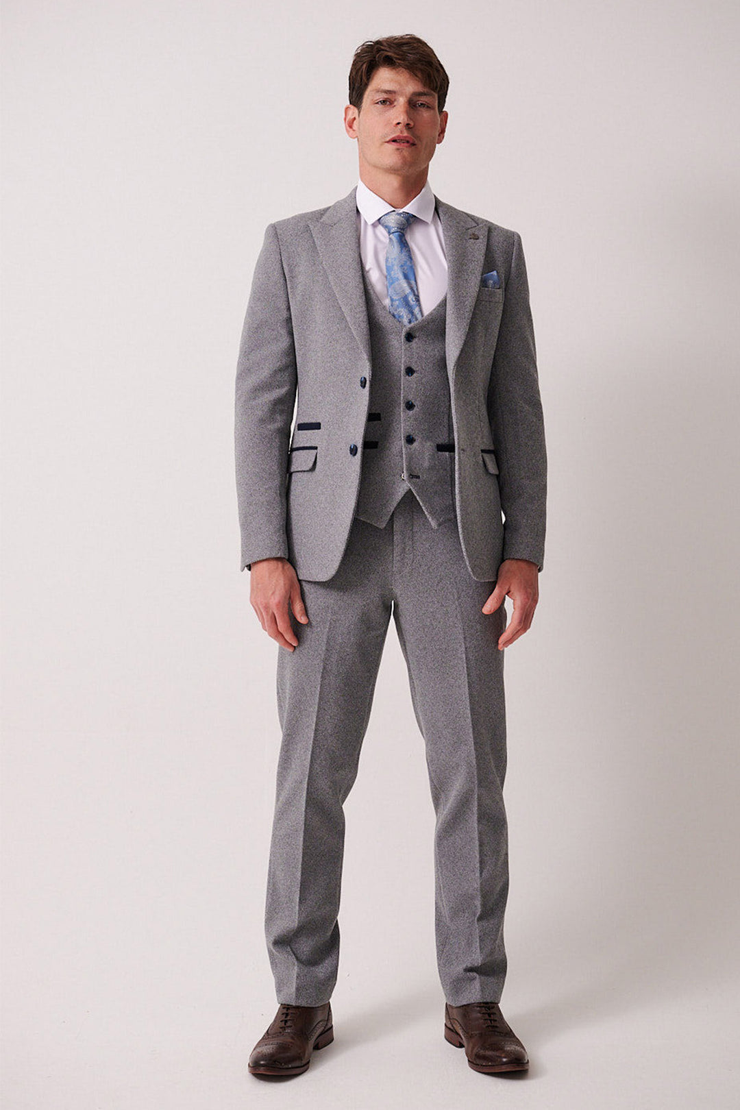 A man models the marcdarcy HAYDEN Silver Blue Crossweave Three Piece Suit against a plain background, paired with a white shirt, blue patterned tie, and brown dress shoes. He stands relaxed with arms at his sides, looking straight ahead.