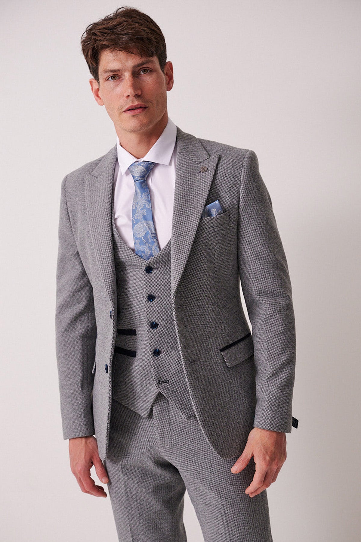A man stands against a plain light background wearing the marcdarcy HAYDEN - Silver Blue Crossweave Blazer, paired with a white dress shirt, blue patterned tie, and matching pocket square.