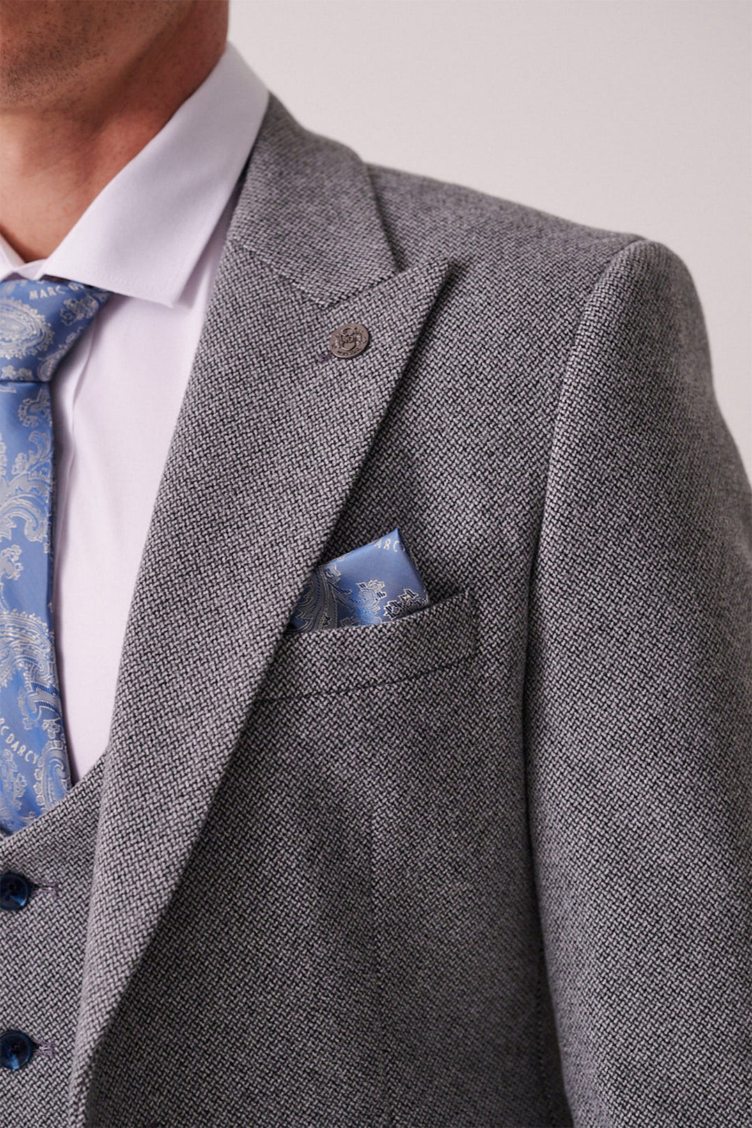 Close-up of a person wearing the marcdarcy HAYDEN Silver Blue Crossweave Three Piece Suit with a white shirt, blue patterned tie, and matching pocket square. Only the upper torso is visible; face partially out of frame.