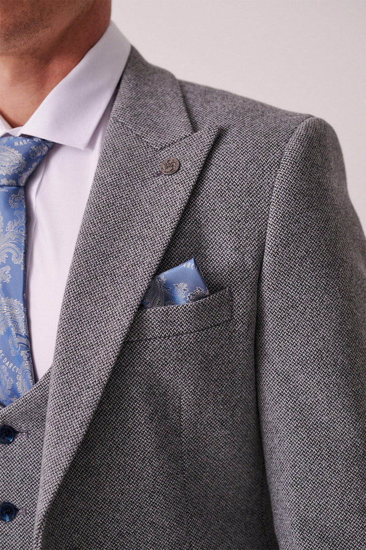 Close-up of a person wearing the marcdarcy HAYDEN Silver Blue Crossweave Three Piece Suit with a white shirt, blue patterned tie, and matching pocket square. Only the upper torso is visible; face partially out of frame.