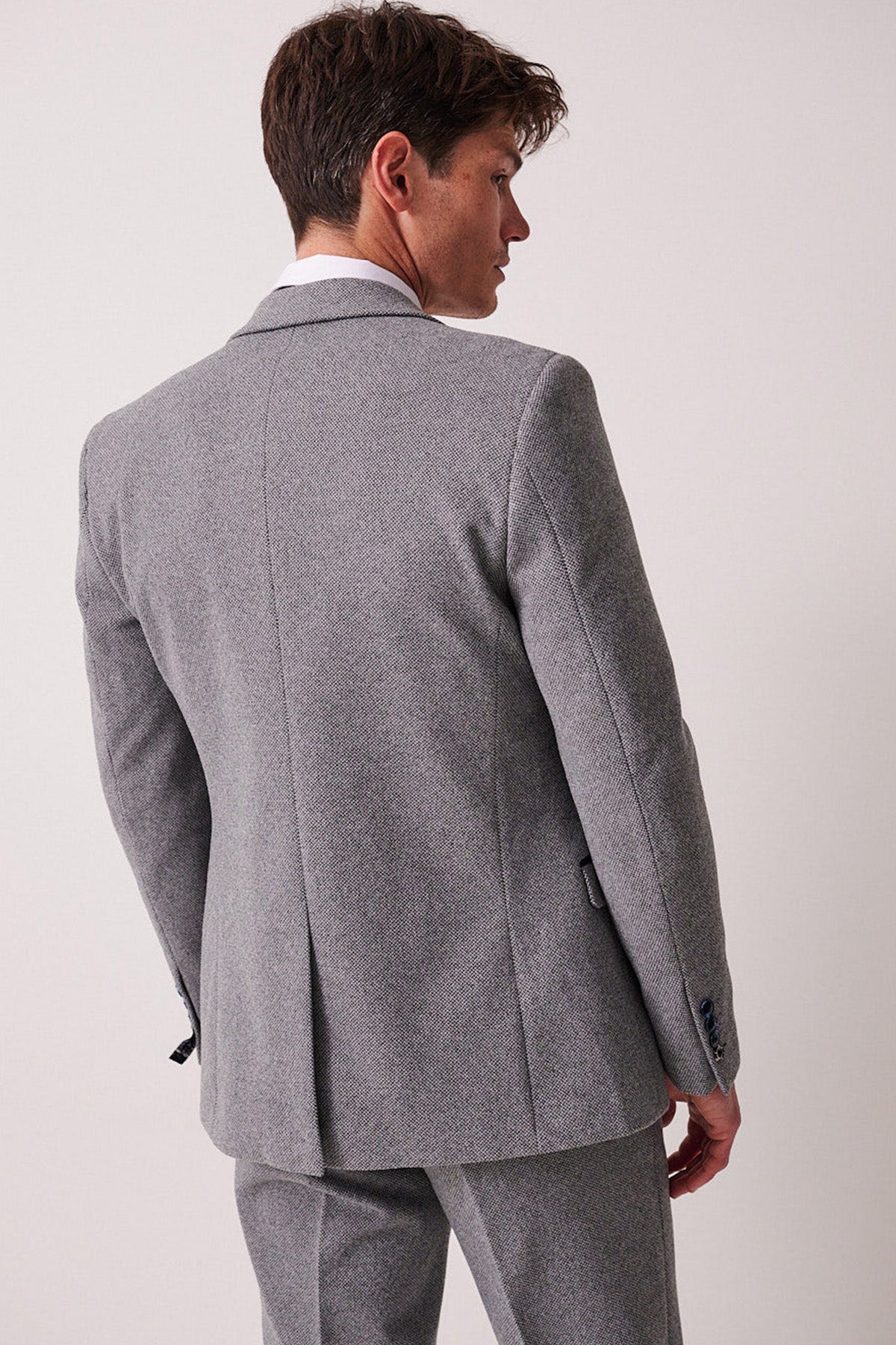 A man with short brown hair wears the marcdarcy HAYDEN Silver Blue Crossweave Three Piece Suit and a white shirt, standing with his back turned and head slightly to the side against a plain light background.