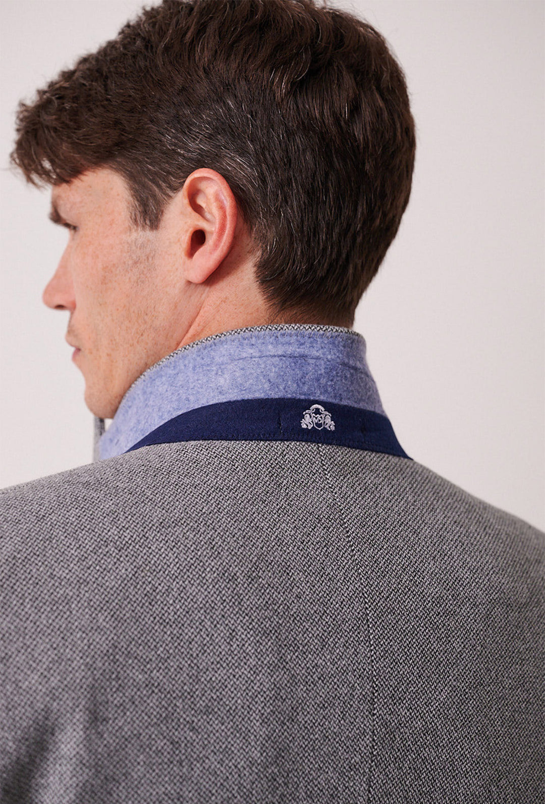 A man is seen from behind in a marcdarcy HAYDEN Silver Blue Crossweave Three Piece Suit, featuring a turned-up blue shirt collar with a small white embroidered emblem.