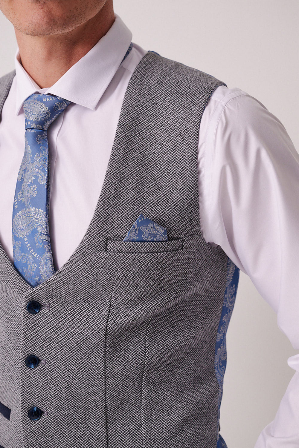 A man wears the Marc Darcy HAYDEN - Silver Blue Crossweave Waistcoat over a white shirt, paired with a blue patterned tie and matching pocket square. The image shows his upper torso, cropped at the mouth and right shoulder.