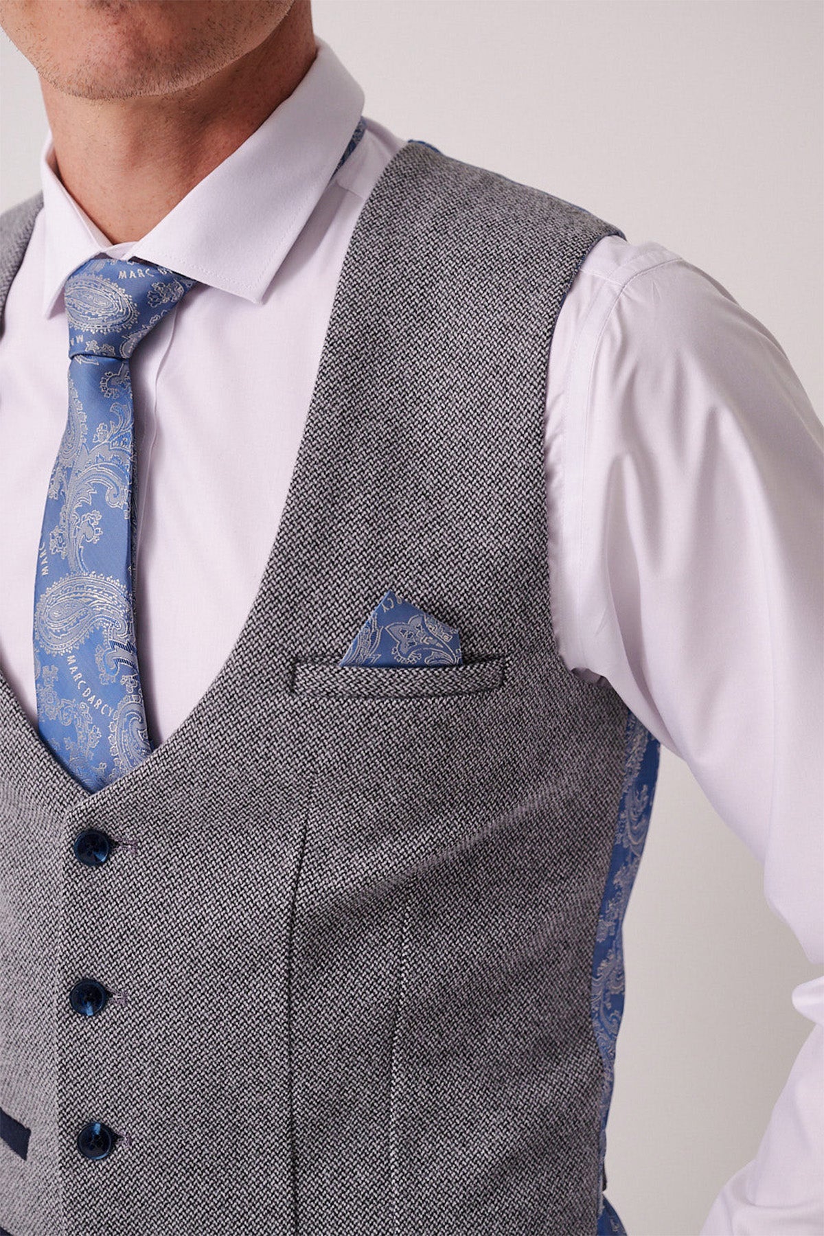 A man wears the Marc Darcy HAYDEN - Silver Blue Crossweave Waistcoat over a white shirt, paired with a blue patterned tie and matching pocket square. The image shows his upper torso, cropped at the mouth and right shoulder.