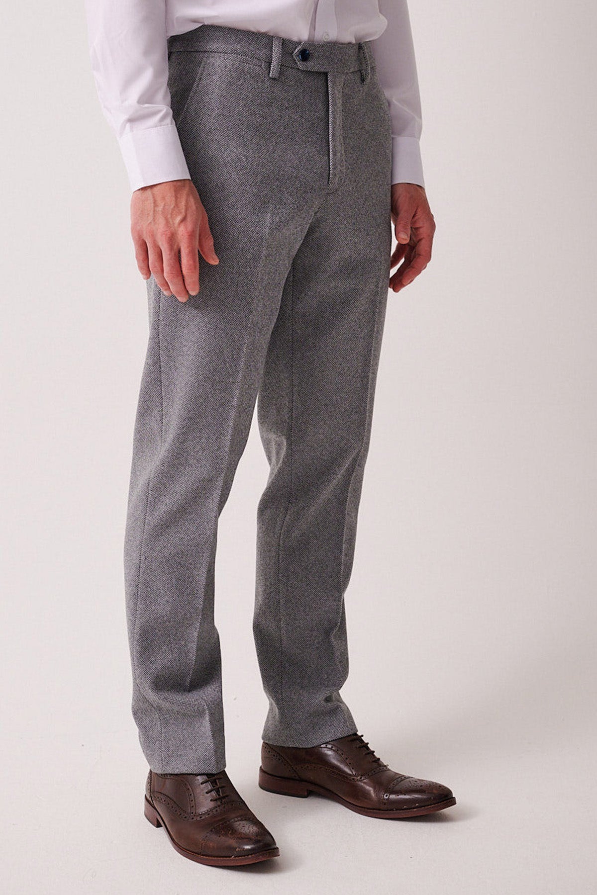 Wearing marcdarcy’s HAYDEN Silver Blue Crossweave Trousers, a white long-sleeve shirt, and brown leather dress shoes, a person stands against a light background, presenting a smart casual style.