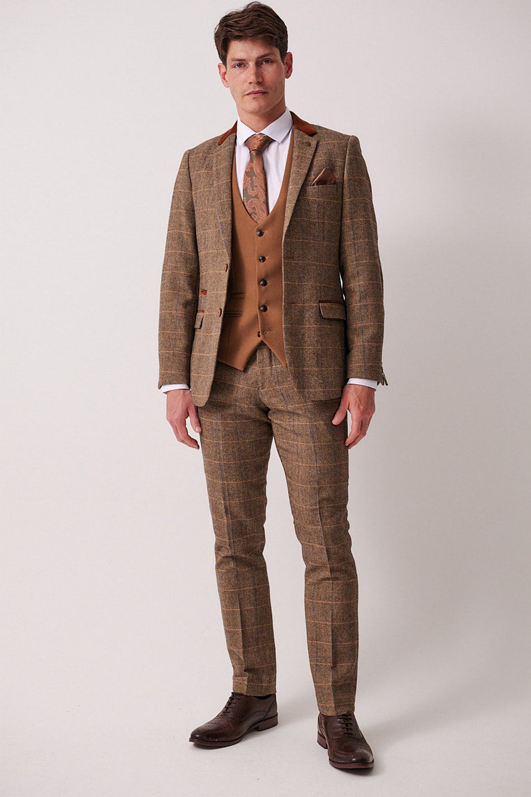 A man stands against a plain background wearing the marcdarcy DX7 Tan Tweed Check Suit with Kelvin Oak Waistcoat, paired with a white shirt, patterned tie, and dark brown dress shoes.
