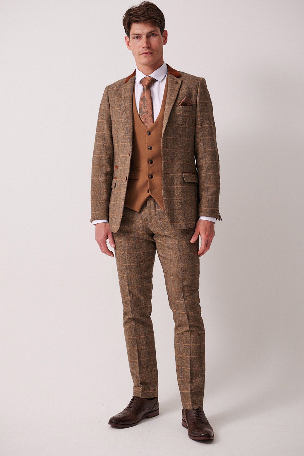 A man stands against a plain background wearing the marcdarcy DX7 Tan Tweed Check Suit with Kelvin Oak Waistcoat, paired with a white shirt, patterned tie, and dark brown dress shoes.