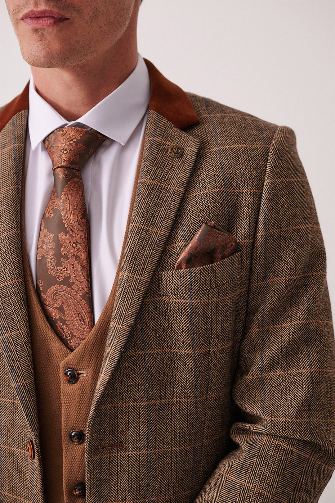A man wears the marcdarcy DX7 Tan Tweed Check Suit with Kelvin Oak Waistcoat, white shirt, paisley brown tie, and brown pocket square—ideal for a country wedding. The image is cropped at the lips.