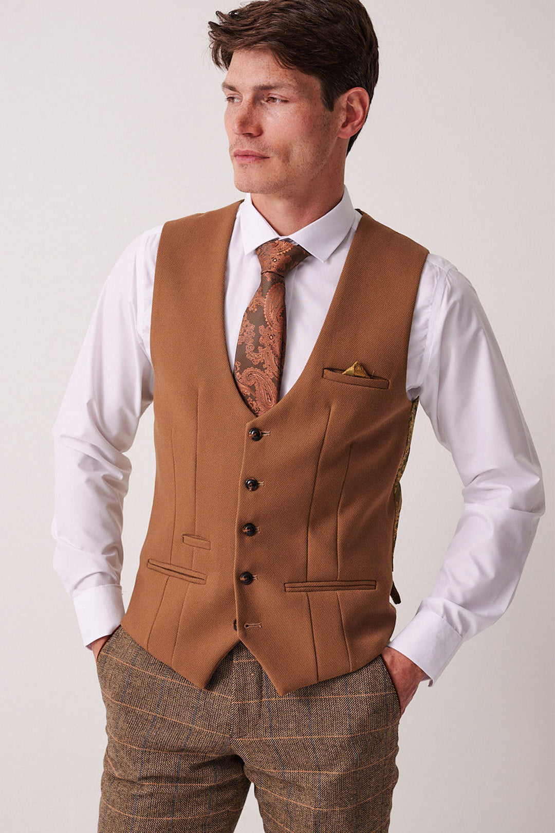 A man in the marcdarcy DX7 - Tan Tweed Check Suit with a Kelvin Oak Waistcoat stands with hands in his pockets, looking to the side.