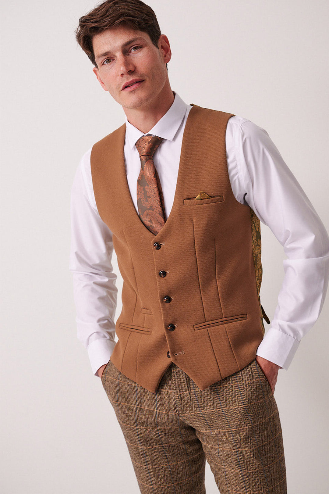 A man wears the marcdarcy DX7 Tan Tweed Check Suit with Kelvin Oak Waistcoat, pairing a white shirt, brown paisley tie, and gold pocket square—ideal for a country wedding.