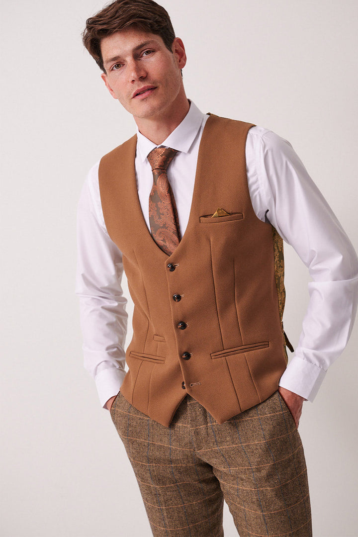 A man wears the marcdarcy DX7 Tan Tweed Check Suit with Kelvin Oak Waistcoat, pairing a white shirt, brown paisley tie, and gold pocket square—ideal for a country wedding.
