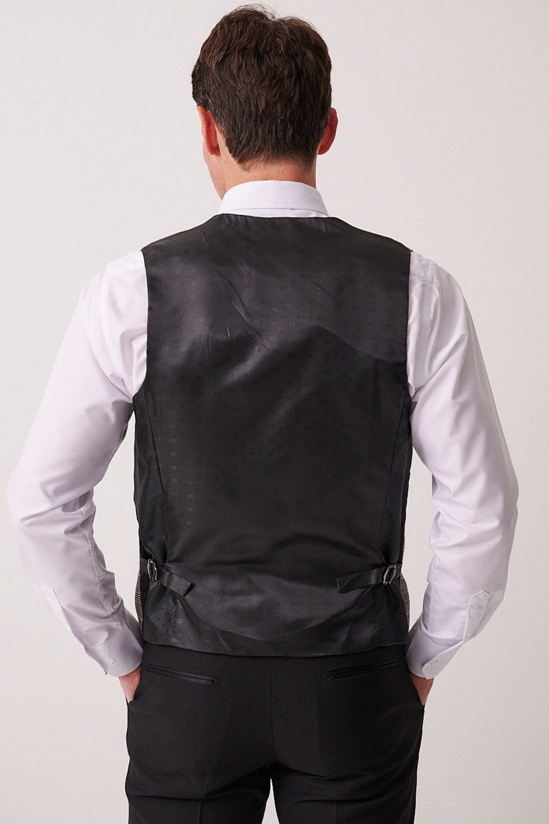 A man wearing the marcdarcy DALTON Black Tux Lapel Suit with Ross Waistcoat stands with his back to the camera, hands on his hips.