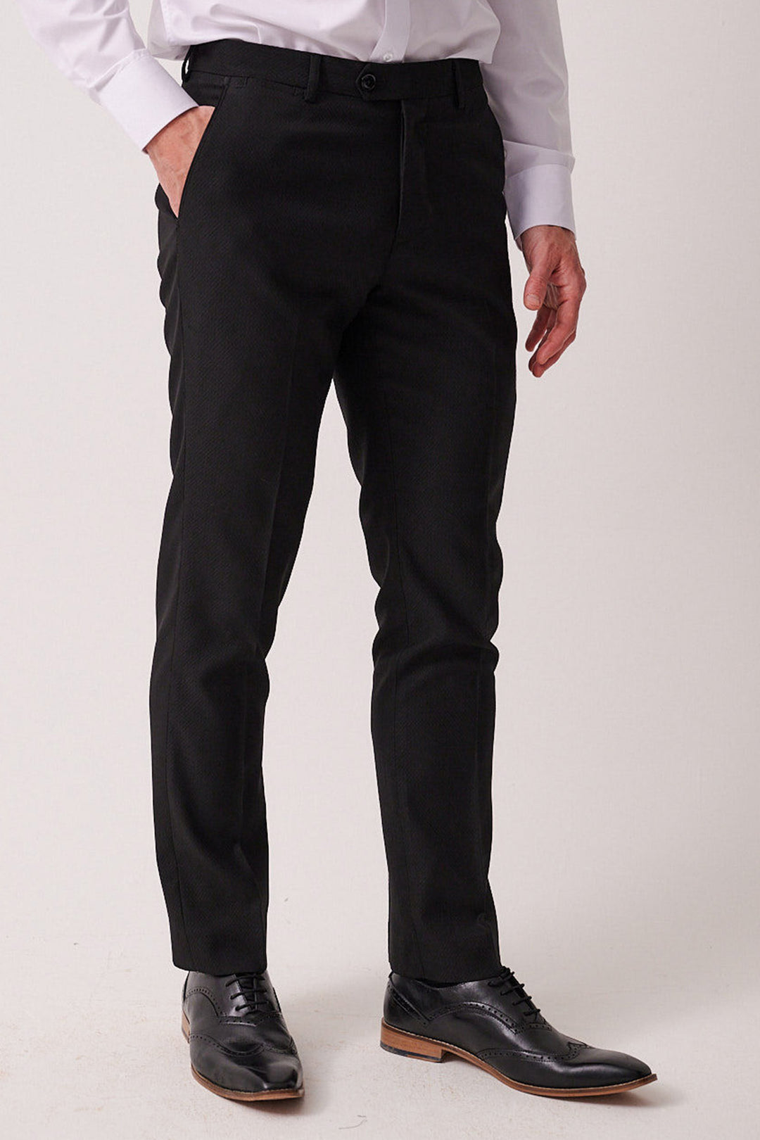 A man in marcdarcy’s DALTON Black Tux Lapel Suit with Ross Waistcoat, paired with a white shirt and black dress shoes. His left hand in his pocket adds a relaxed touch to this sophisticated monochrome look, perfect for black tie events.
