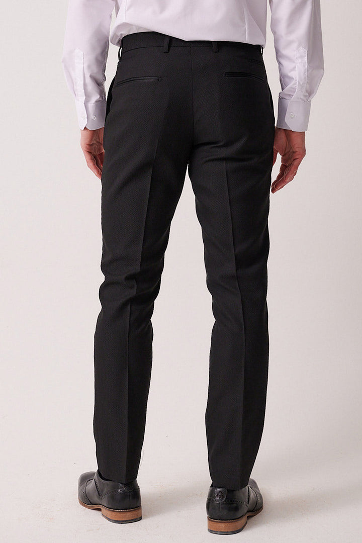 A man in a marcdarcy DALTON black tux lapel suit with Ross waistcoat stands facing away against a plain light background, highlighting the timeless elegance of this monochrome ensemble.