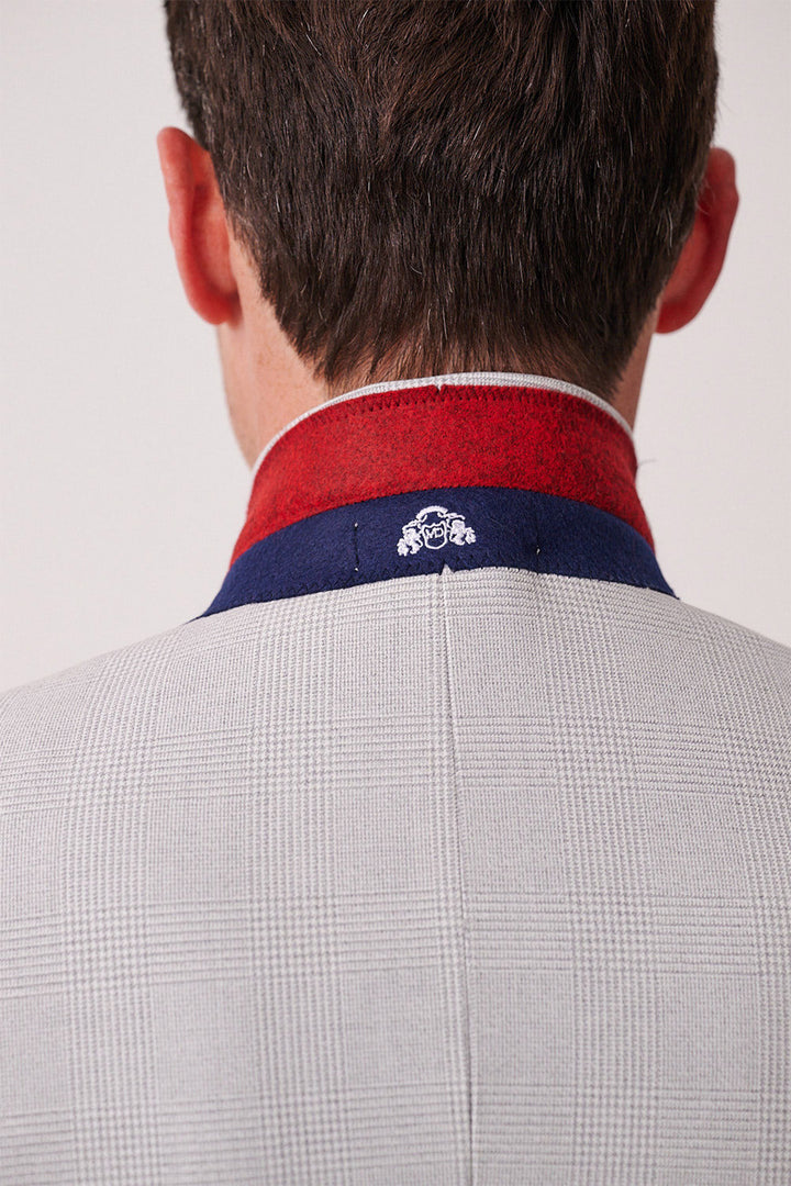 Back view of a man wearing the Marc Darcy BROMLEY Stone Check Suit with Kelvin Sky Waistcoat. The slim fit jacket features a dark blue and red collar with a white embroidered logo.