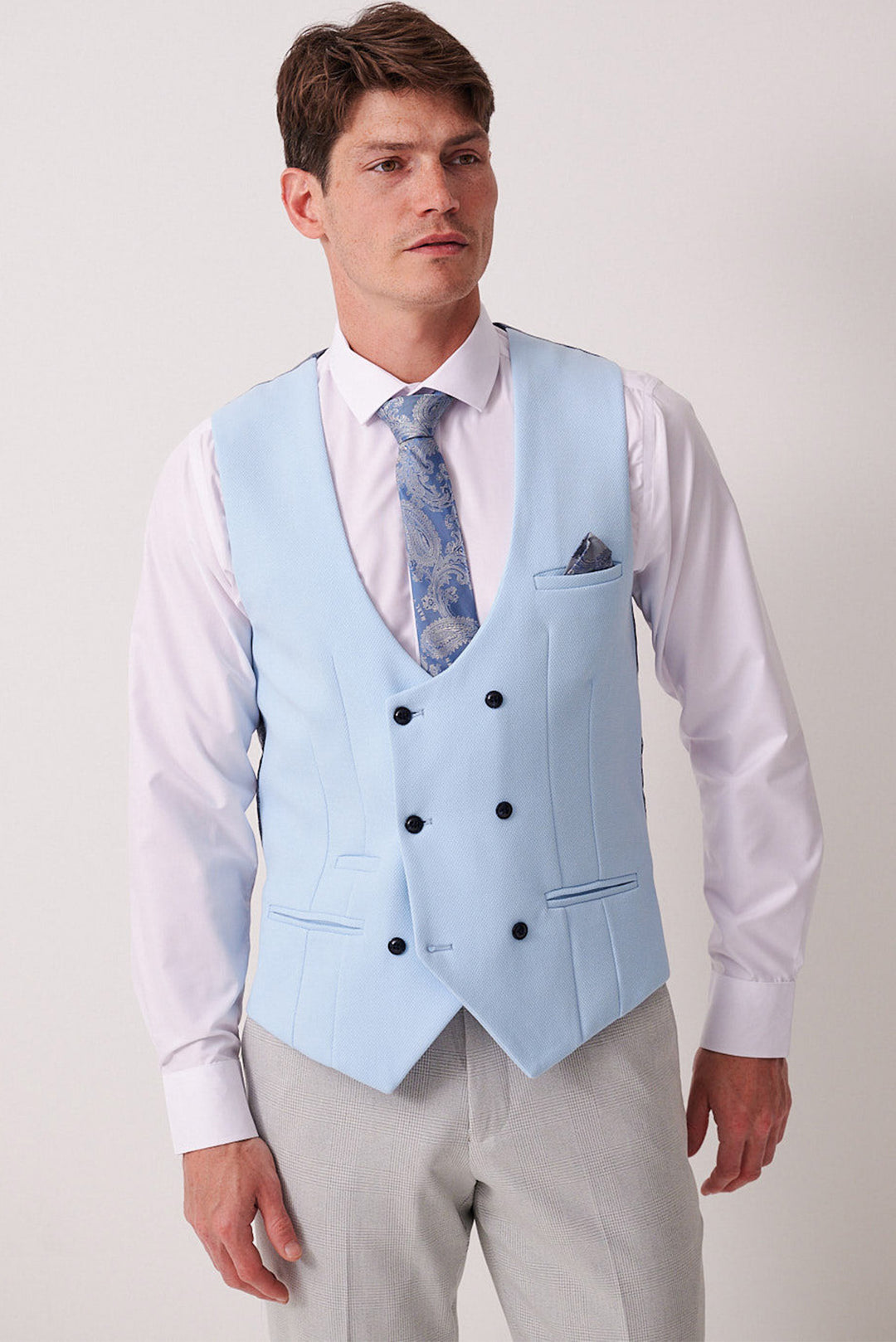 A man wears the Marc Darcy BROMLEY Stone Check Suit with Kelvin Sky Waistcoat—a refined spin on the classic three-piece look, featuring a light blue waistcoat, patterned tie, and Prince of Wales check trousers.