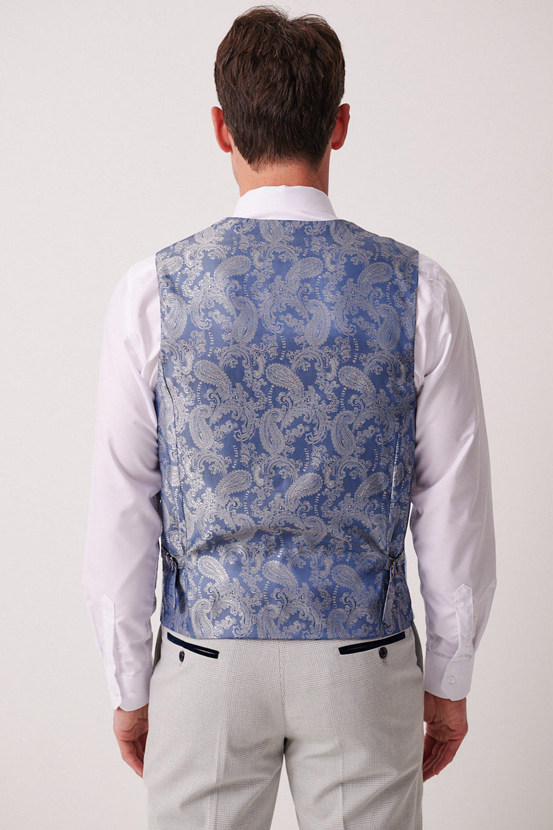 A man facing away wears the Marc Darcy BROMLEY stone check suit pants with the Kelvin Sky paisley waistcoat over a white shirt.