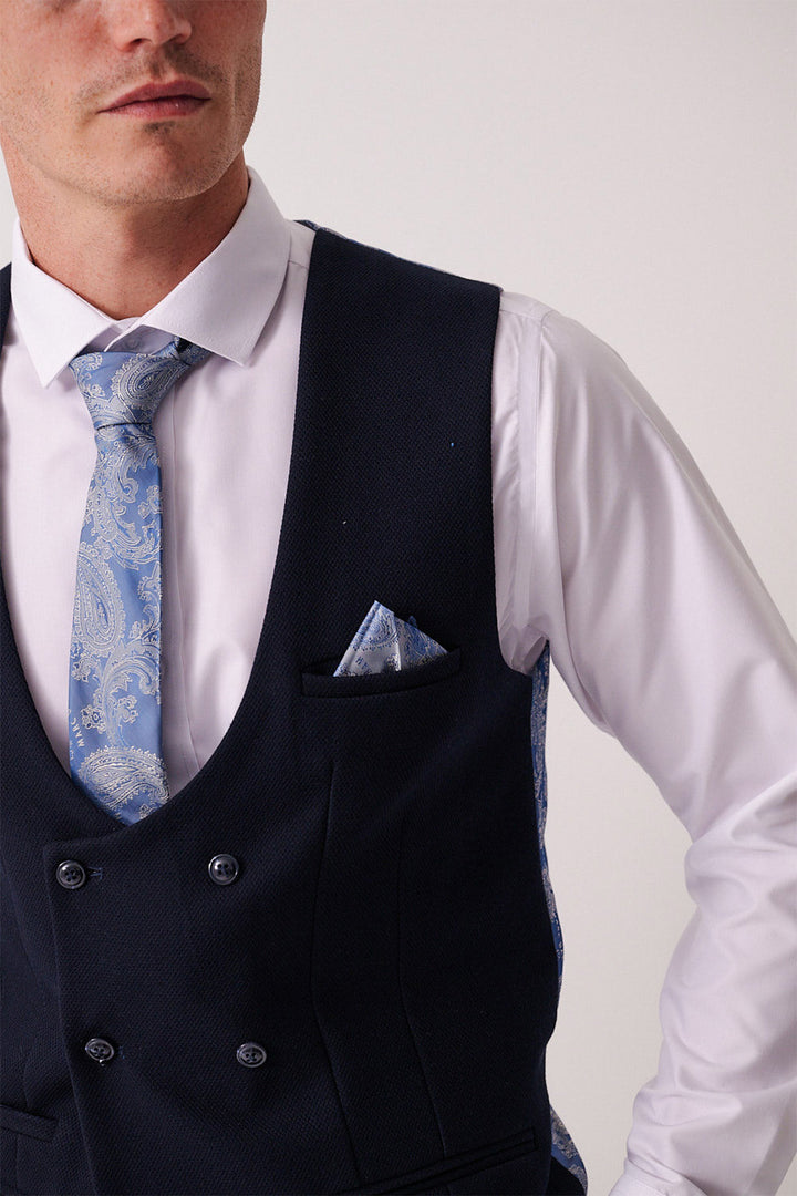 A man in a Marc Darcy BROMLEY Stone Check Suit with a Kelvin Navy Waistcoat wears a white dress shirt and light blue paisley tie, with a matching pocket square in his waistcoat. His face is partially visible.