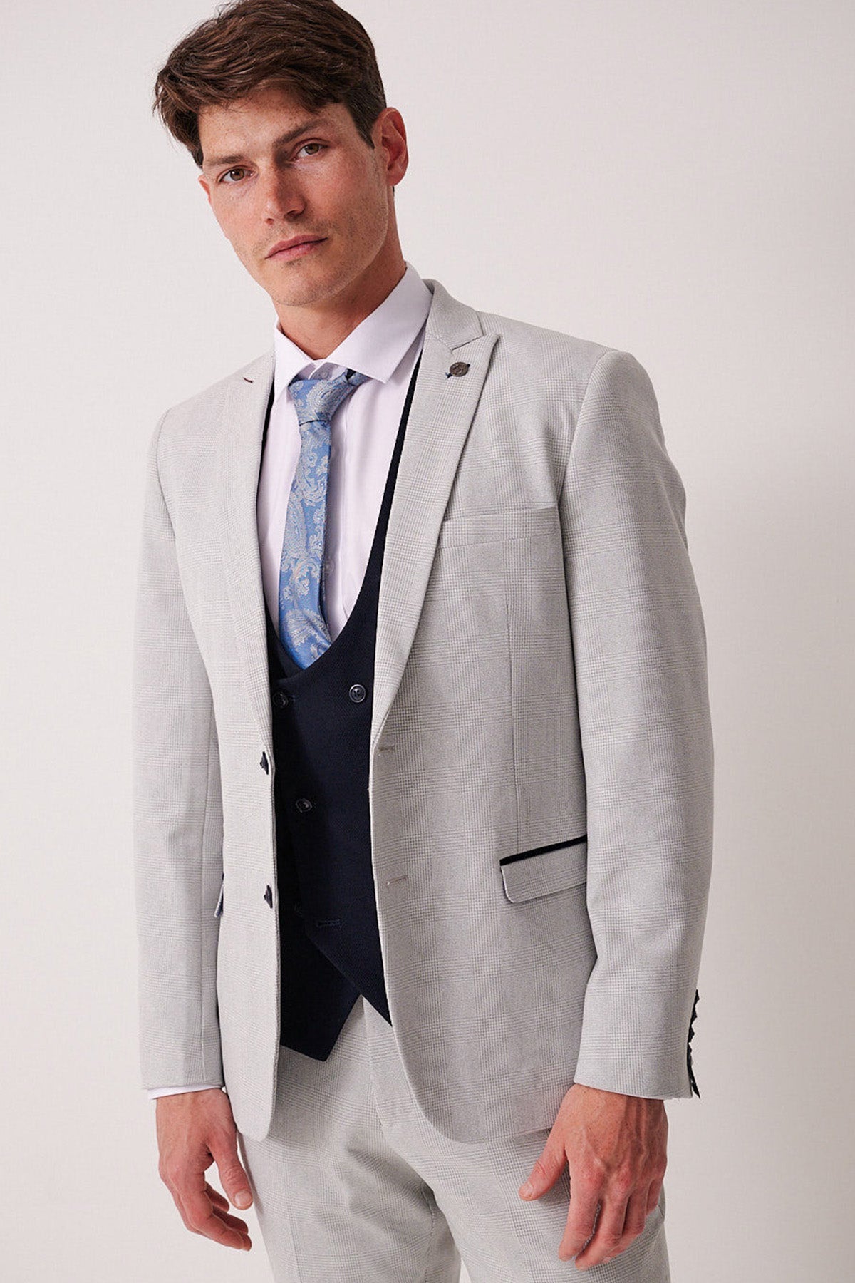 A man wearing the Marc Darcy BROMLEY Stone Check Suit with a Kelvin Navy Waistcoat and a light blue paisley tie.
