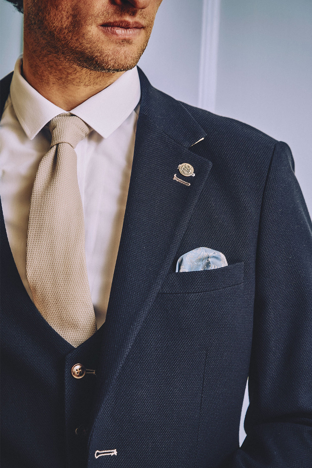 A man is shown from the shoulders down wearing the marcdarcy MD7 - Navy Blue Blazer, styled in a slim fit. He pairs it with a white dress shirt, beige tie, patterned pocket square, and a lapel pin on his formal jacket.