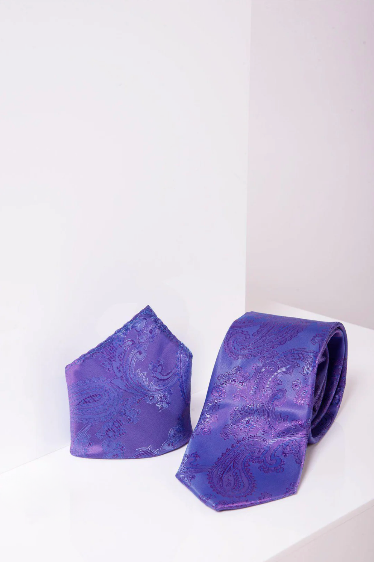 The Marc Darcy PAISLEY - Lilac Paisley Tie and Pocket Square Set, featuring a folded pocket square and matching paisley tie, is displayed on a white surface with a light-colored background.