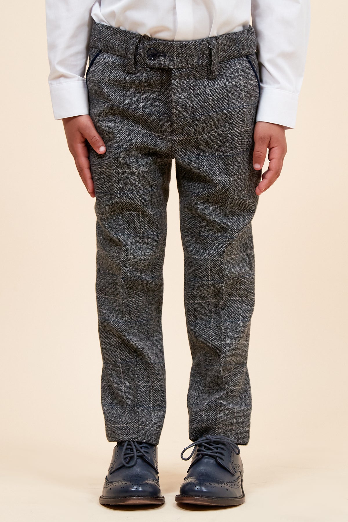 A child wears the marcdarcy SCOTT Grey Check Three Piece Suit, featuring an adjustable waistband, paired with a white long-sleeve shirt and dark blue brogue shoes, standing hands by their sides against a neutral background.