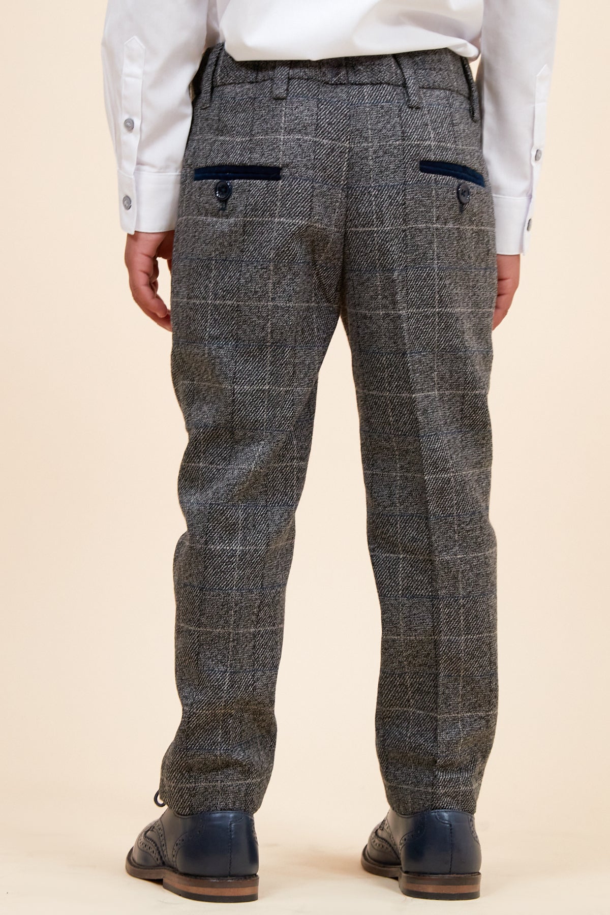 A child, seen from the back, wears the marcdarcy SCOTT Childrens Grey Check Three Piece Suit with adjustable-waist pants featuring two back pockets with dark trim, paired with dark blue dress shoes.