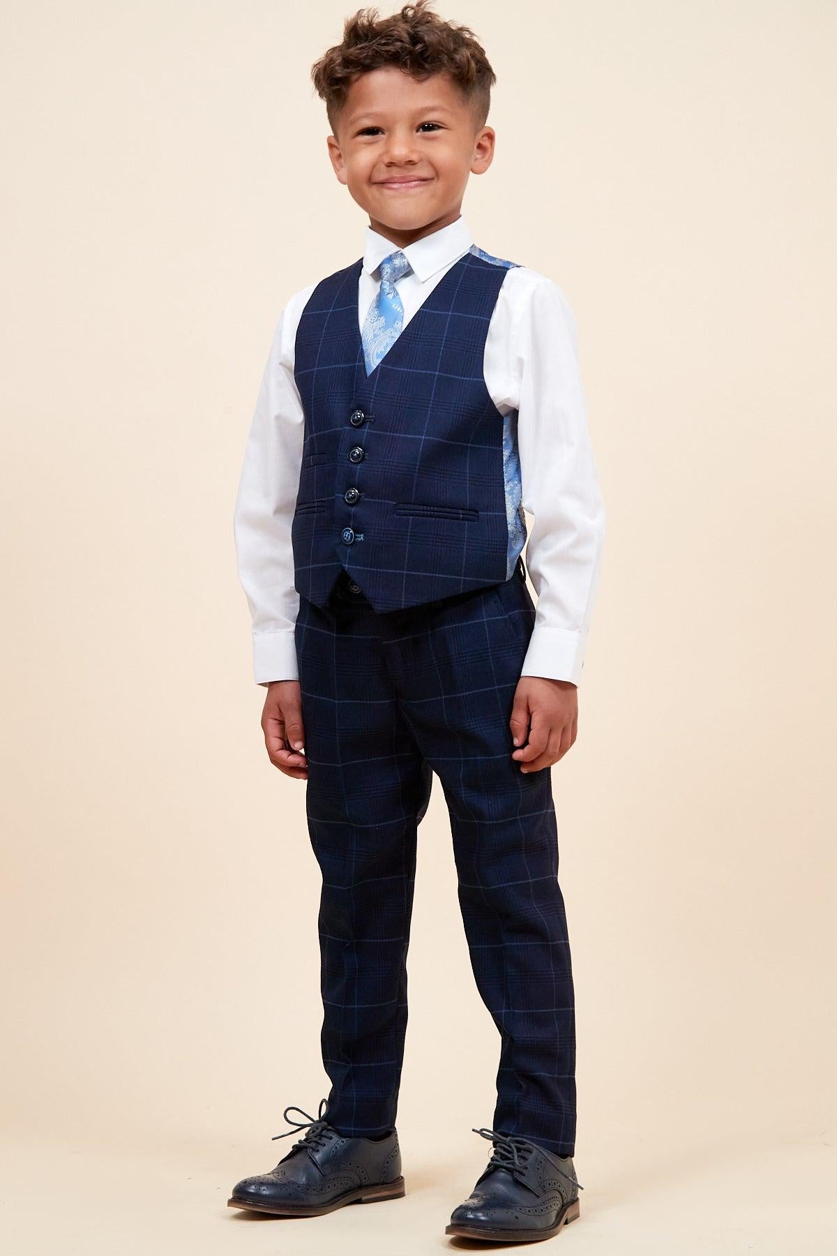 A young boy smiles in the Marc Darcy EDINSON Children's Navy Sky Check Print Three Piece Suit, featuring a matching vest, white shirt, and blue tie—perfect as a stylish kids wedding suit against a plain beige background.