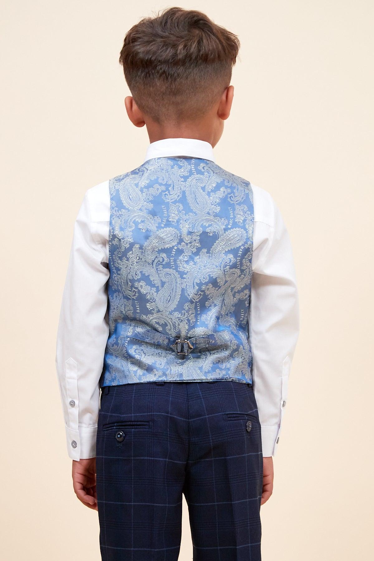 A young boy with neatly trimmed hair is seen from behind in Marc Darcy’s EDINSON Children’s Navy Sky Check Print Three Piece Suit, featuring a light blue vest, white shirt, and navy plaid trousers against a plain beige background.