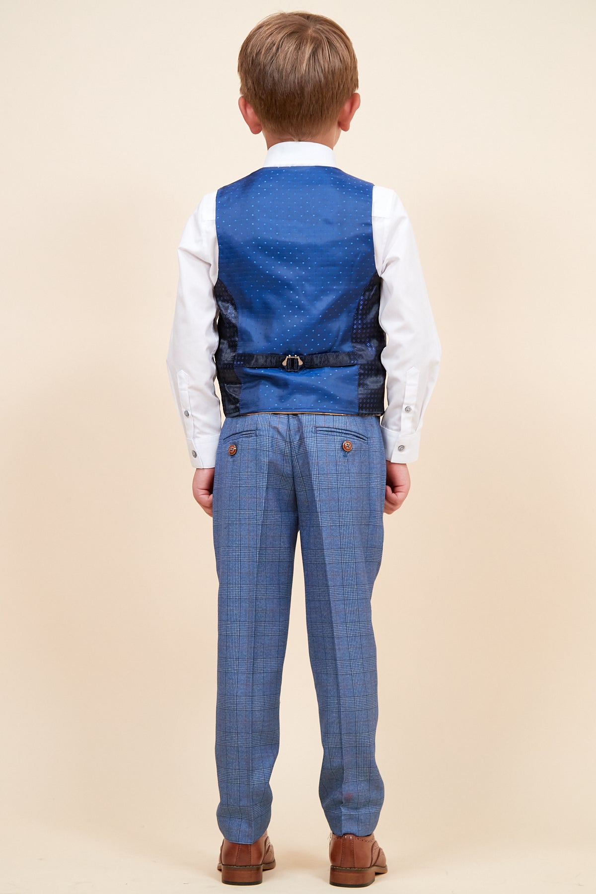 A young boy is seen from behind wearing the marcdarcy GEORGE Childrens Light Blue Check Three Piece Suit, featuring a white shirt and checked waistcoat, standing on a light background in formal attire.