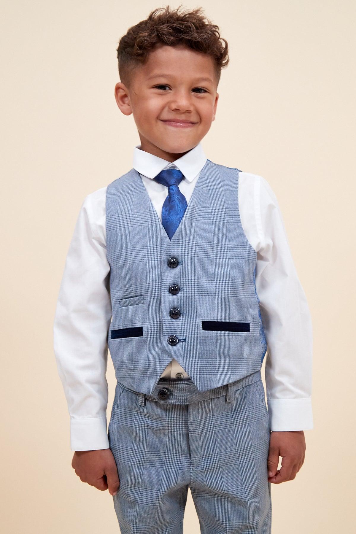 A young boy smiles in the Marc Darcy BROMLEY Children's Sky Blue Check Print Three Piece Suit—a stylish white shirt, blue check vest, patterned tie, and matching pants.