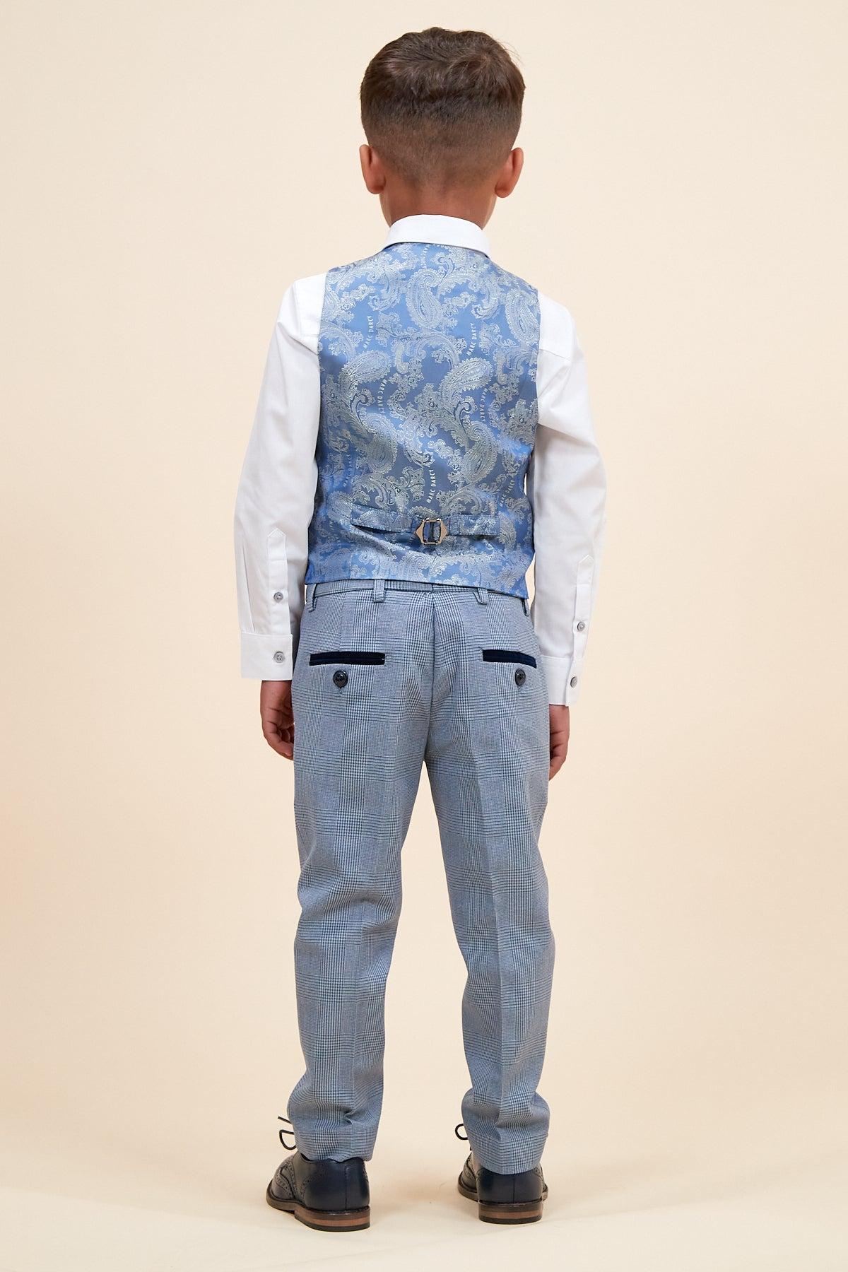 A young boy poses formally with his back to the camera, wearing the Marc Darcy BROMLEY Children's Sky Blue Check Print Three Piece Suit against a plain beige background. His hands rest by his sides.