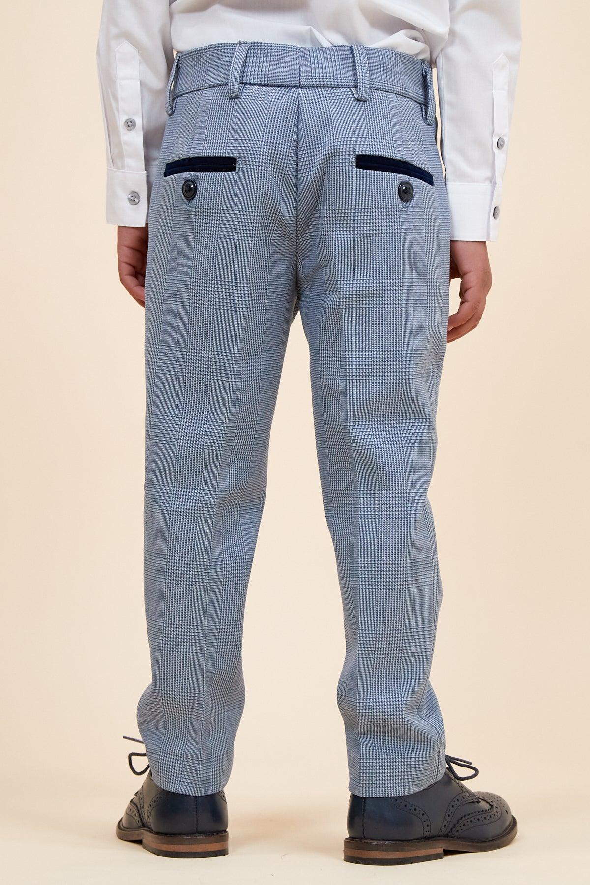A child is shown from the back wearing the Marc Darcy BROMLEY Children's Sky Blue Check Print Three Piece Suit, featuring a light blue check pattern, with a white shirt and dark dress shoes, standing against a beige background.