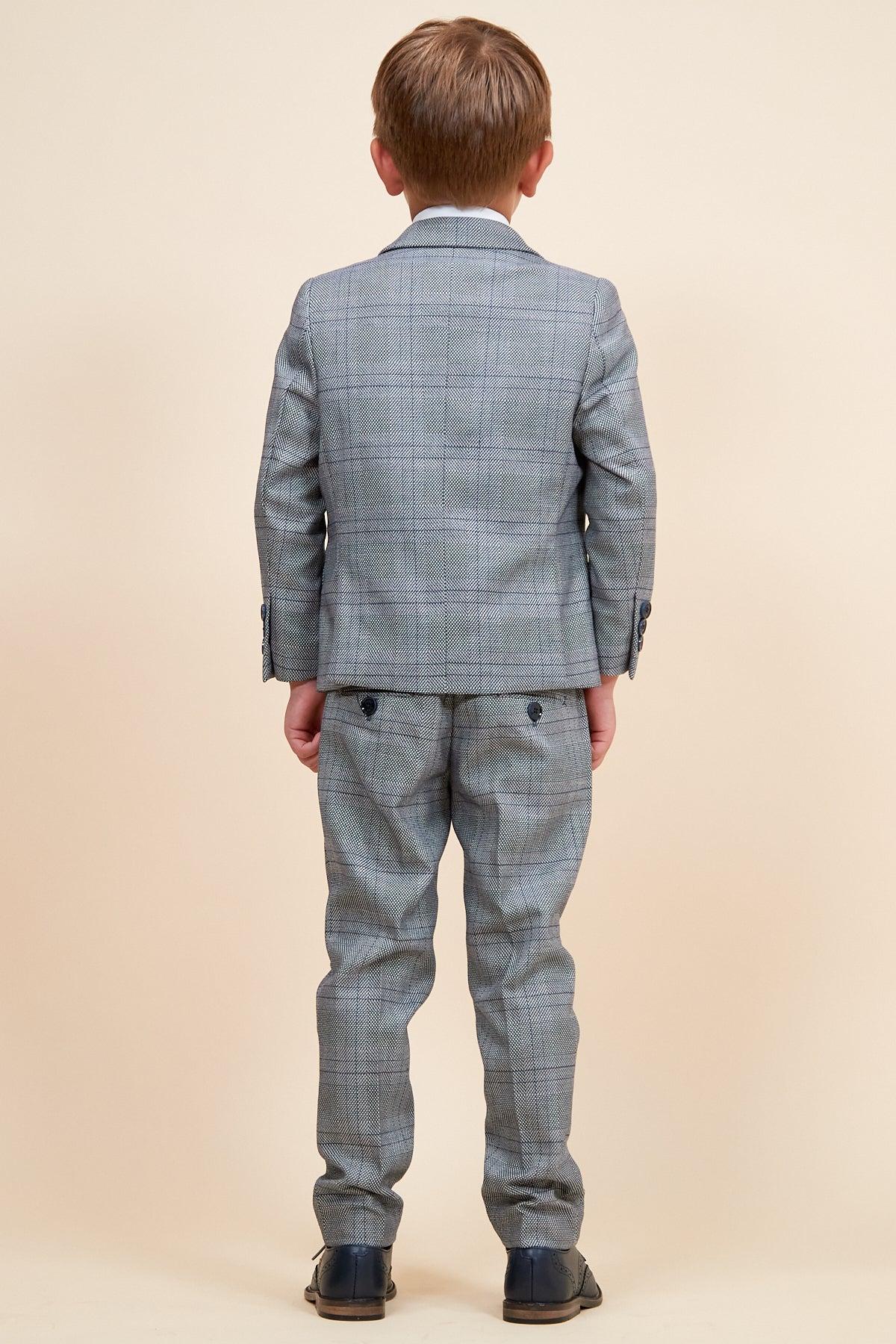 A boy is seen from the back wearing the marcdarcy JERRY Children's Grey Check Three Piece Suit with an adjustable waistband, a white shirt, and dark shoes, set against a cream background.