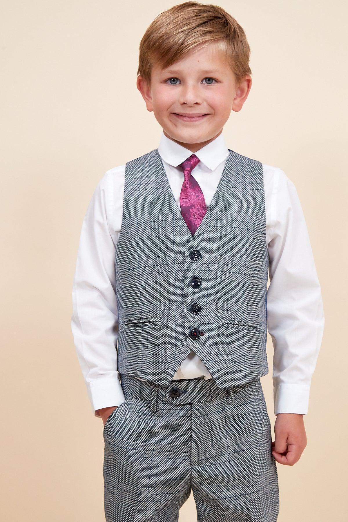 A smiling boy wears the marcdarcy JERRY - Childrens Grey Check Three Piece Suit, featuring an adjustable waistband, white dress shirt, grey check vest and pants, and a pink paisley tie.
