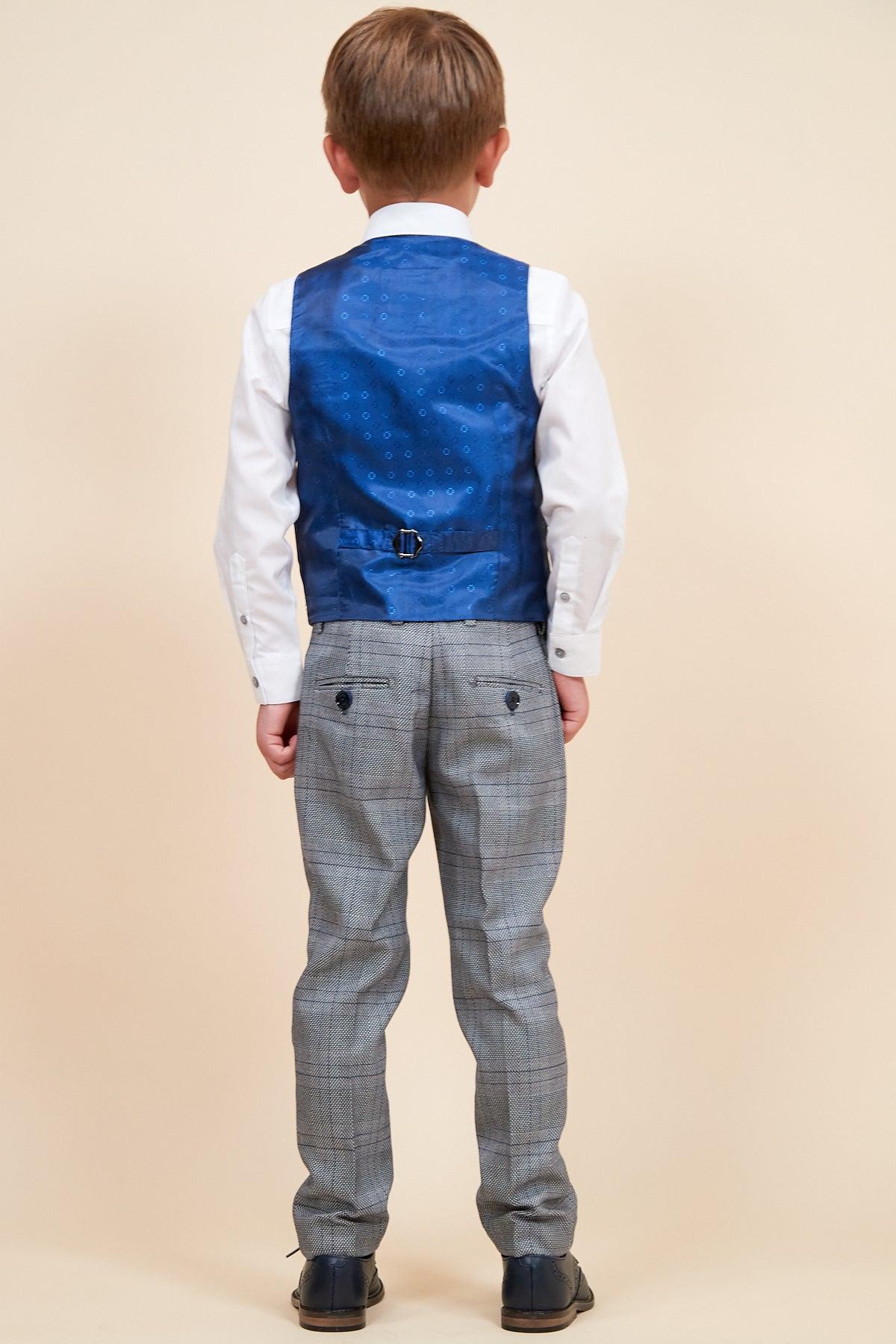 A young boy, seen from behind, wears the marcdarcy JERRY Childrens Grey Check Three Piece Suit with an adjustable waistband—featuring a blue vest, white shirt, and plaid trousers—paired with black shoes against a plain beige background.