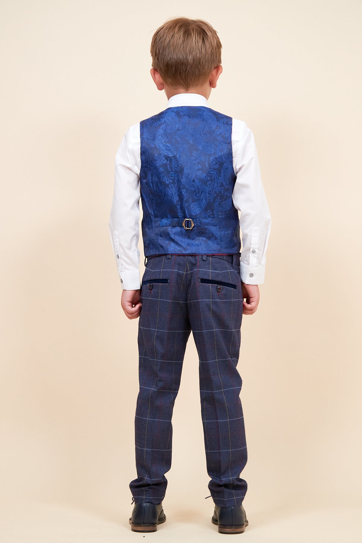 Back view of a boy in the marcdarcy DRAKE Children's Navy Check Three Piece Suit, featuring a white shirt, blue patterned vest, and plaid pants with adjustable waistband—stylish and comfortable.