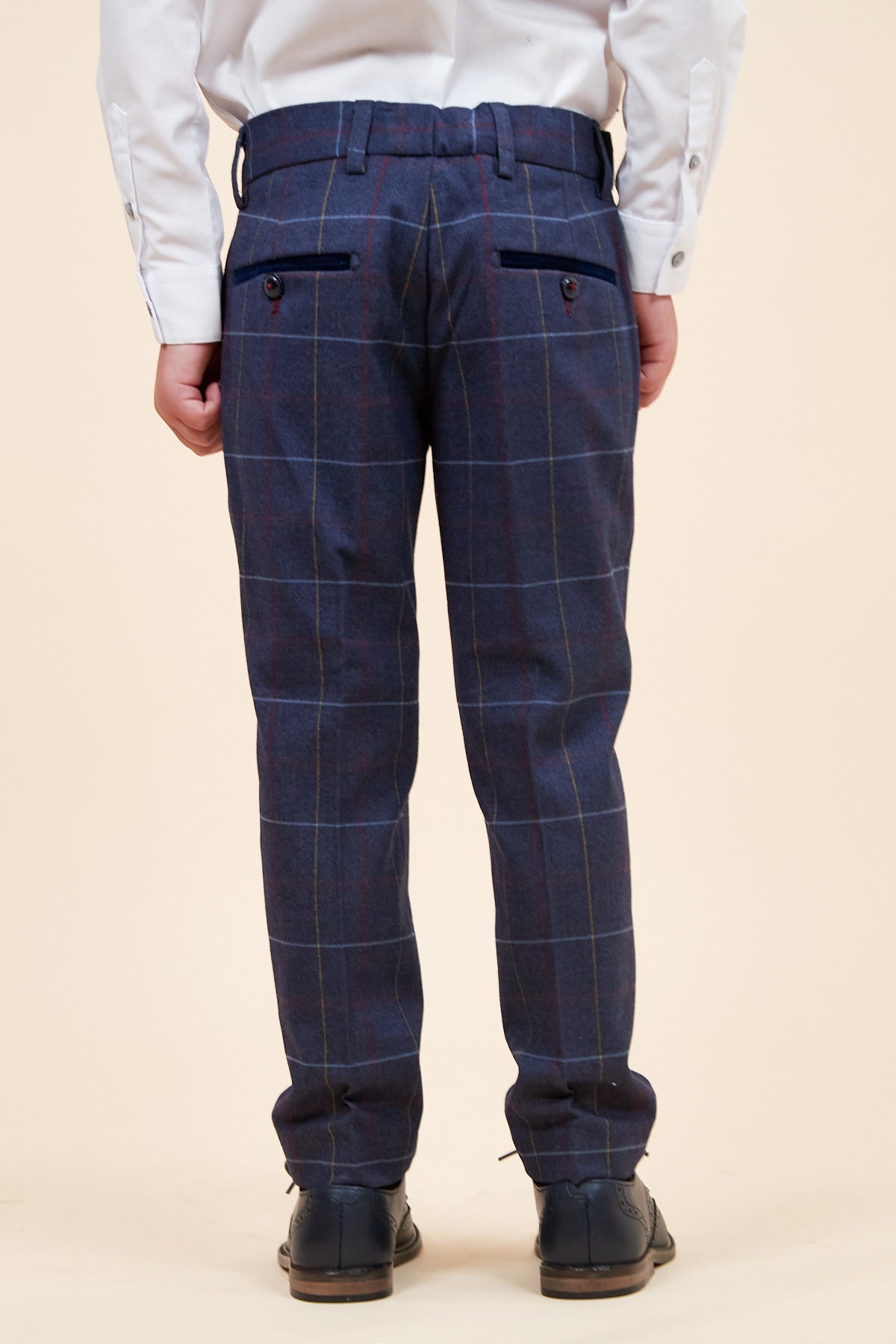 A child wearing the marcdarcy DRAKE Childrens Navy Check Three Piece Suit faces away from the camera in a classic pageboy style, paired with a white shirt and black shoes against a plain beige background.