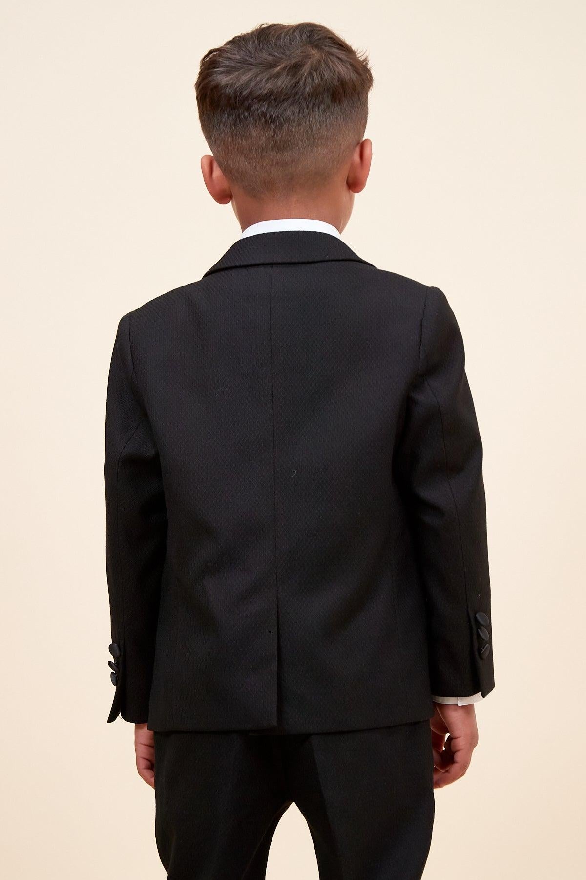 A young boy with short brown hair stands with his back to the camera, wearing the marcdarcy DALTON Children's Black Tux Lapel Diamond Three Piece Suit against a plain, light-colored background.