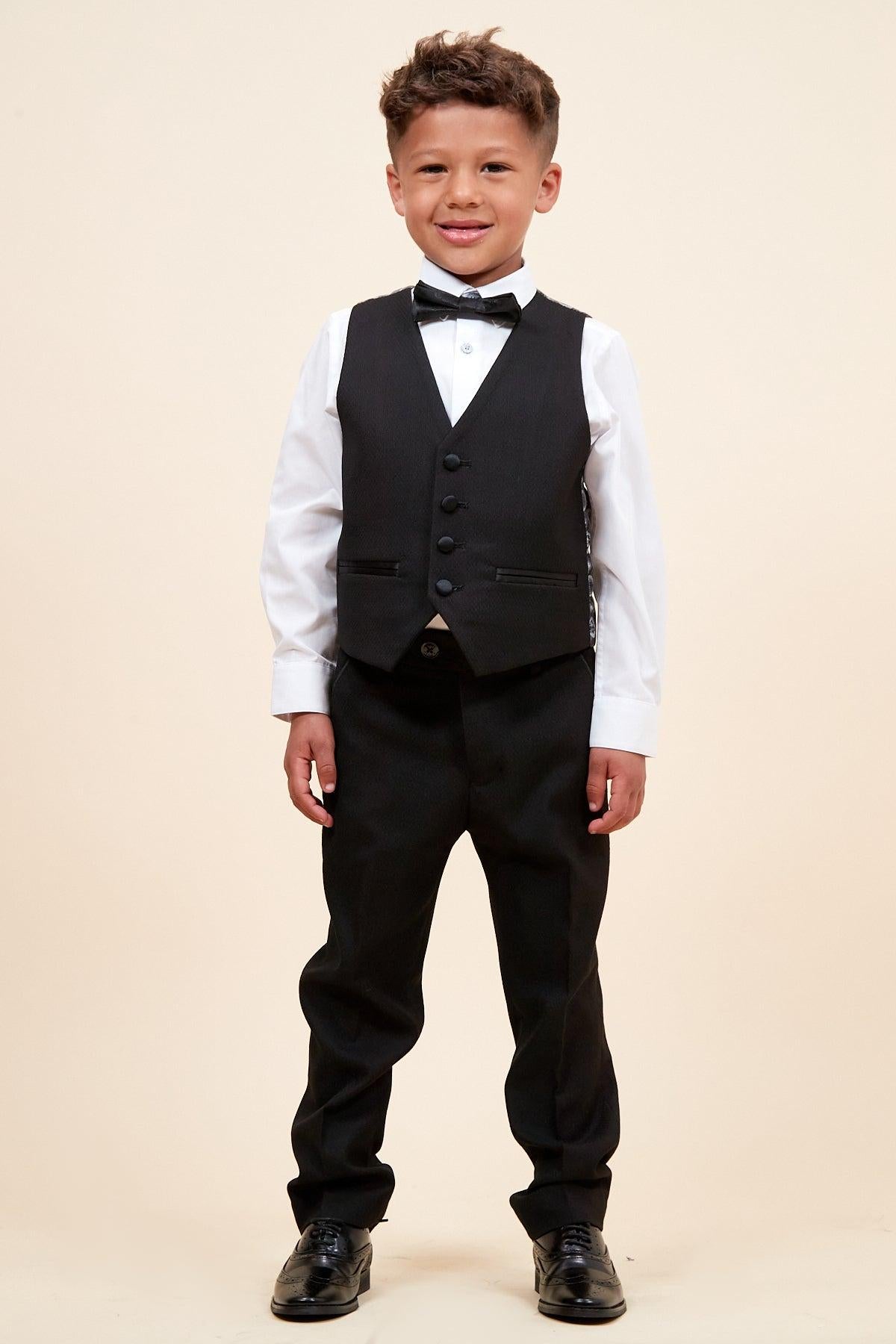 A young boy smiles at the camera wearing the marcdarcy DALTON Children's Black Tux Lapel Diamond Three Piece Suit, paired with a crisp white shirt and black bow tie.